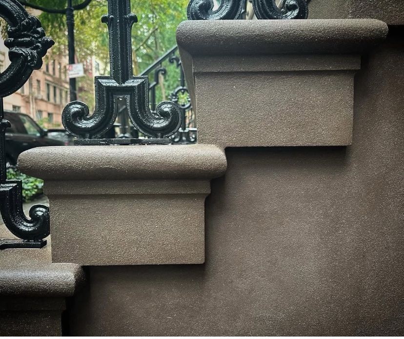 Close-up of brownstone steps with ornate black wrought iron railing in urban setting.